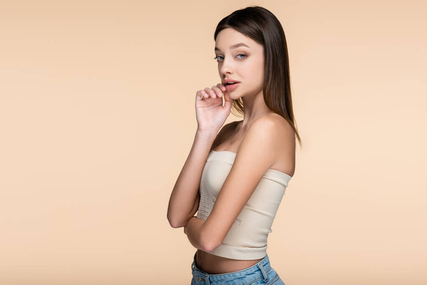 brunette and pretty woman in crop top looking at camera isolated on beige  - Foto, afbeelding