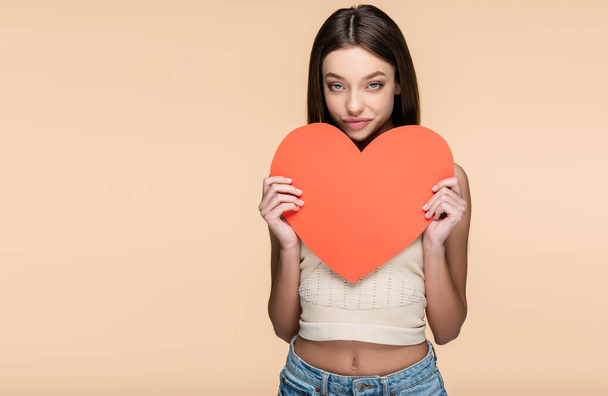 brunette woman in crop top holding paper heart isolated on beige  - Фото, изображение