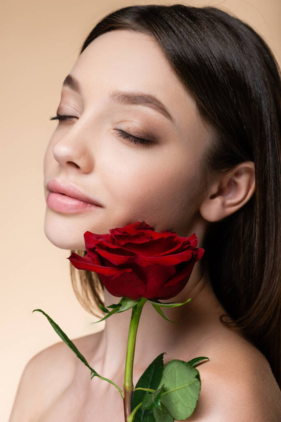 young woman with closed eyes near rose isolated on beige  - Foto, imagen