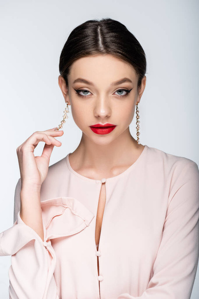 pretty woman with red lips looking at camera while touching earring isolated on grey - Fotografie, Obrázek