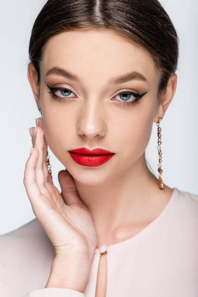 pretty woman in earrings with red lips looking at camera isolated on grey - 写真・画像