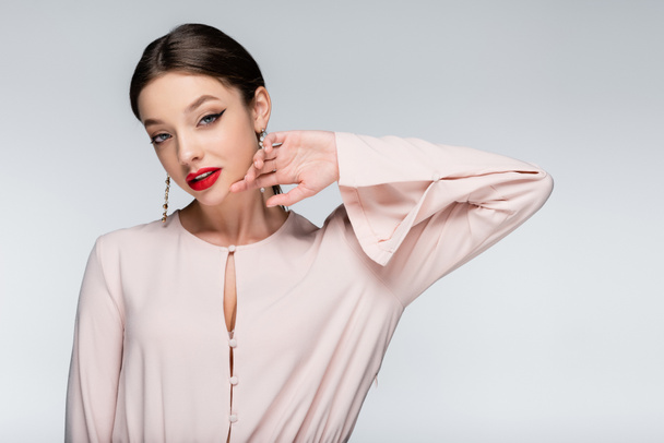 brunette woman in earrings and blouse looking at camera while posing isolated on grey - Foto, Imagem