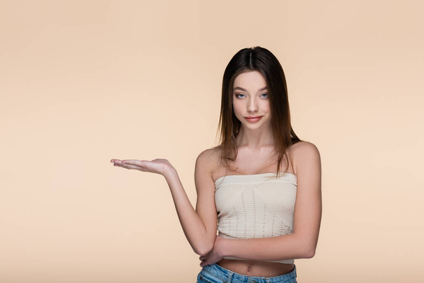 young and pretty woman in crop top pointing with hand isolated on beige  - Photo, image