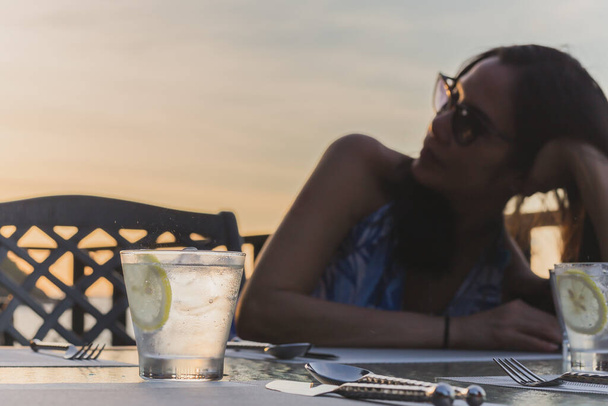 Bril van gezonde voeding sprankelend water en schijfje citroen met vrouw op de achtergrond. - Foto, afbeelding