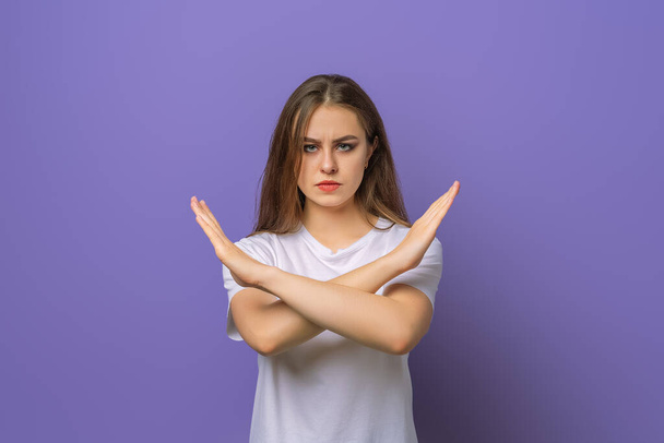 Serious girl showing stop cross gesture, disapprove something, prohibit action, make taboo no sign, standing over purple background. Young emotional woman in purple hoodie - Photo, Image