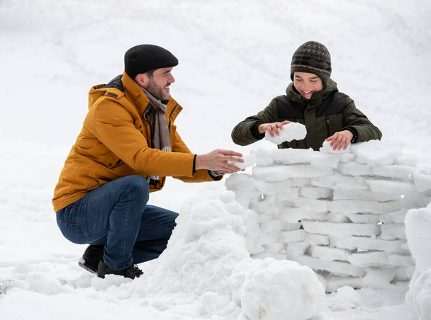 Father and son playing on snow, building structure on snow frozen bricks in park - Zdjęcie, obraz