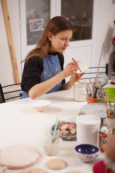 Fotografía vertical de una artista femenina decorando un cuenco de cerámica en un estudio de cerámica - Foto, imagen