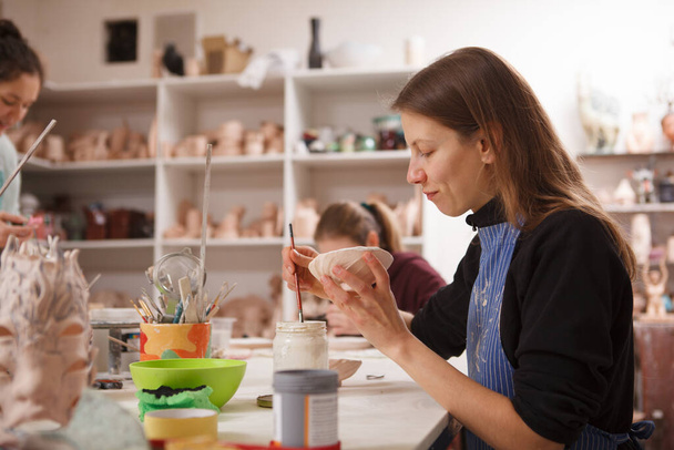 Woman decorating ceramic bowl, enjoying working at pottery studio, copy space - Photo, image