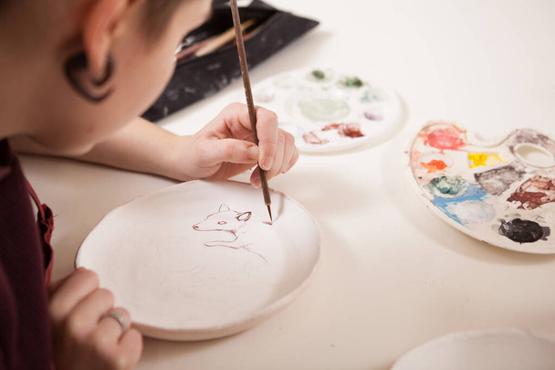 Cropped rear view close up of a female artist painting on a ceramic plate - 写真・画像