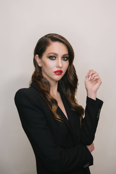 Elegant portrait of young sexy beautiful woman with perfect skin makeup red lips, eyeshadows, eyelashes wearing black jacket on gray background - 写真・画像