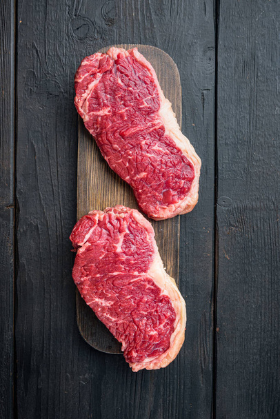 Sirloin steak, nyers marhahús vágás, fekete fa háttér, felülnézet - Fotó, kép