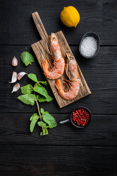 Jumbo shrimps on wooden board with herbs over black wood table, top view, flat lay, food photo. - Фото, изображение
