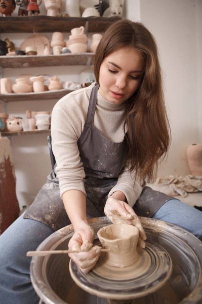 Vertical shot of a beautfiful woman working at pottery class, using potters wheel - Foto, afbeelding