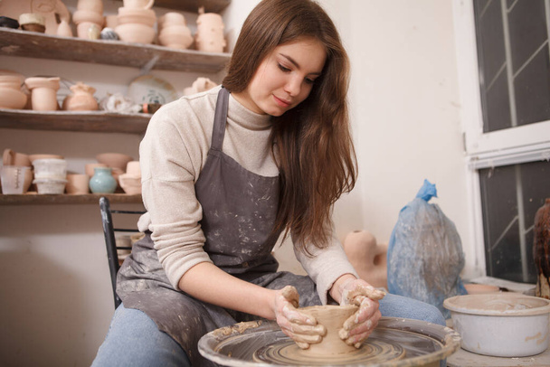 Attractive female potter shaping clay bowl on potters wheel - Foto, afbeelding
