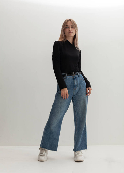portrait of a beautiful blonde in a black turtleneck and jeans on a light background - Foto, Imagem