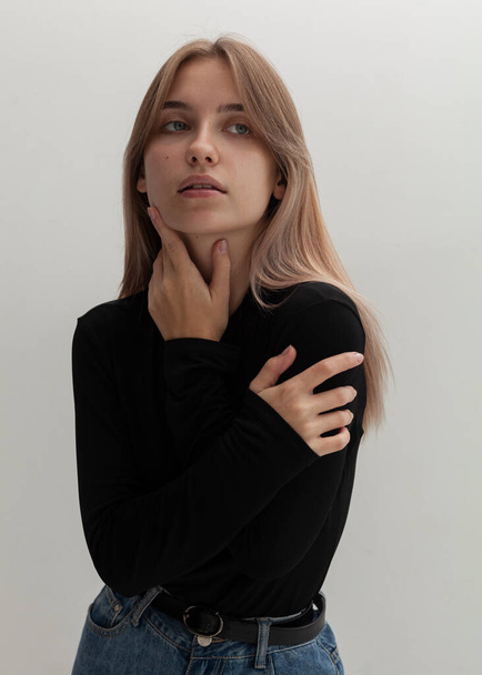 portrait of a beautiful blonde in a black turtleneck and jeans on a light background - Фото, изображение