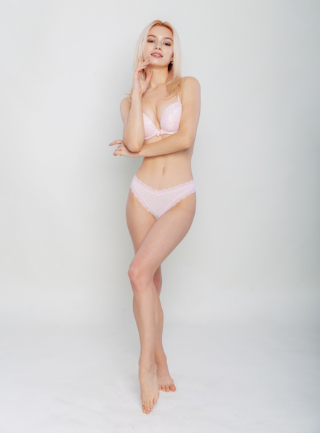Full length woman model in lingerie. Beautiful slender blonde wearing sexy pink underwear clean smooth healthy skin isolated over light gray background. Hair removal, spa or lingerie advertisement. - 写真・画像