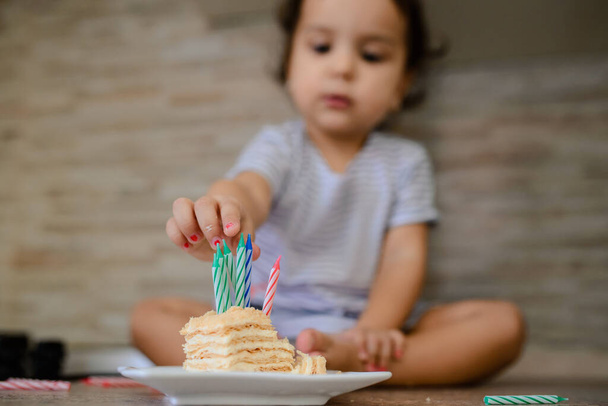 Κοντινό πλάνο του μικρού κοριτσιού να βάζει κεριά σε ένα κομμάτι κέικ. Επιλεκτική εστίαση - Φωτογραφία, εικόνα