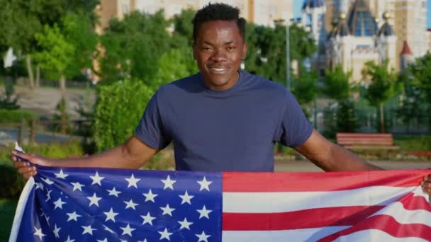 Μεγέθυνση κάμερας σε πατριώτη χαμογελώντας Αφρο-Αμερικανός άνδρας κρατώντας αμερικανική σημαία - Πλάνα, βίντεο