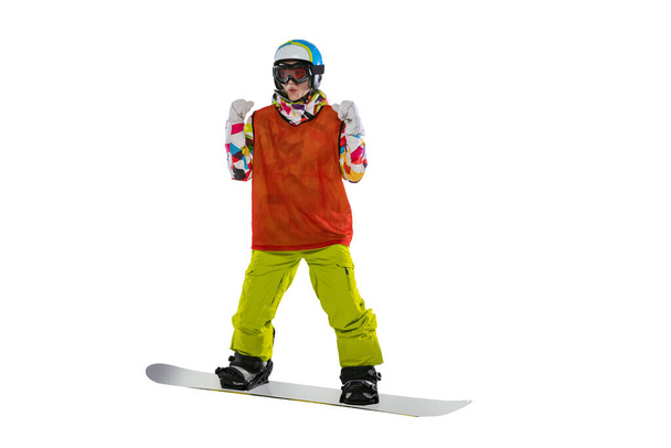 Happy young girl in bright sportswear, goggles and helmet standing with snowboard isolated on white studio background. Concept of winter sports - Foto, Bild