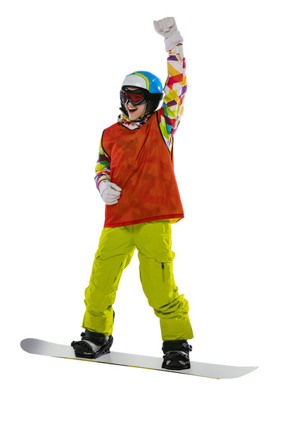 Happy young girl in bright sportswear, goggles and helmet standing with snowboard isolated on white studio background. Concept of winter sports - Фото, изображение