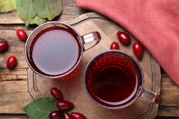 Glass cups of fresh dogwood tea, berries and leaves on wooden table, flat lay - Foto, afbeelding