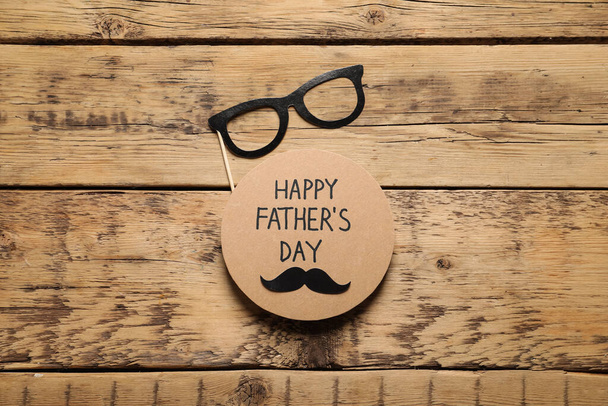 Card with phrase Happy Father's Day and paper glasses on wooden background, flat lay - Photo, image