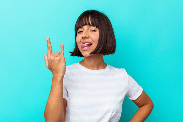 Young mixed race woman isolated on blue background showing rock gesture with fingers - Photo, Image