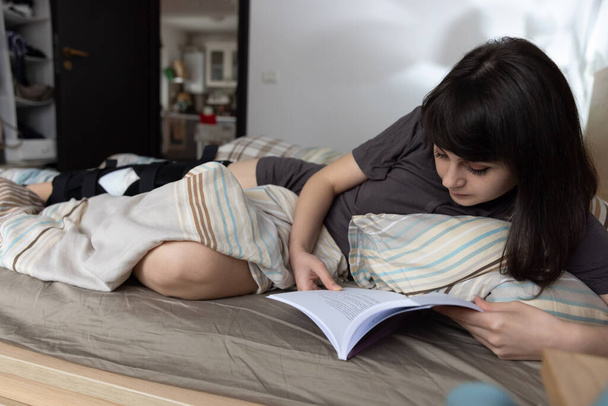 ACL ameliyatı olan bir kadın evde yatakta kitap okuyor.. - Fotoğraf, Görsel