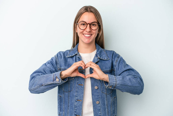 Young caucasian woman isolated on blue background smiling and showing a heart shape with hands. - Foto, immagini