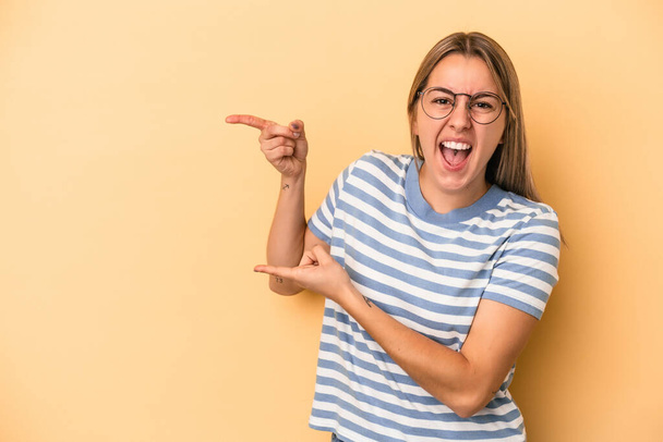 Young caucasian woman isolated on yellow background excited pointing with forefingers away. - Photo, Image