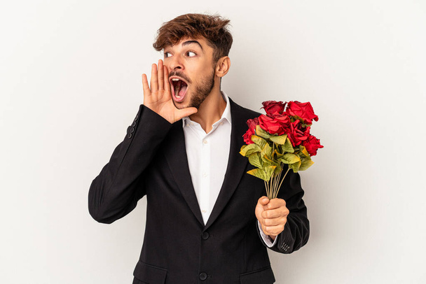 Joven hombre de raza mixta sosteniendo ramo de rosas aisladas sobre fondo blanco gritando y sosteniendo la palma cerca de la boca abierta. - Foto, imagen