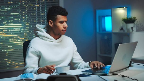 bel homme multiracial boire une tasse de café et travailler sur ordinateur la nuit
 - Photo, image