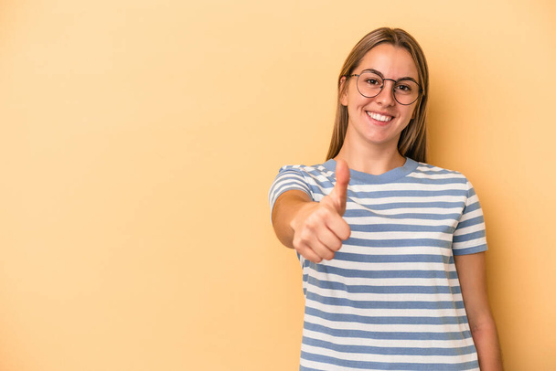 Young caucasian woman isolated on yellow background smiling and raising thumb up - 写真・画像