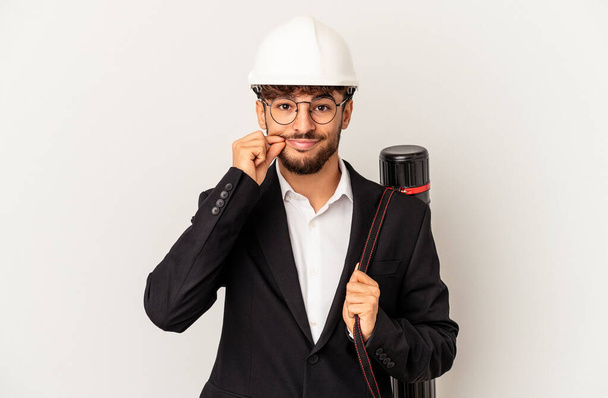 Young mixed race architect man wearing a helmet isolated on grey background with fingers on lips keeping a secret. - Photo, Image