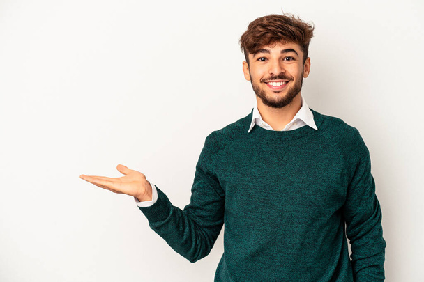 Young mixed race man isolated on grey background showing a copy space on a palm and holding another hand on waist. - Foto, immagini