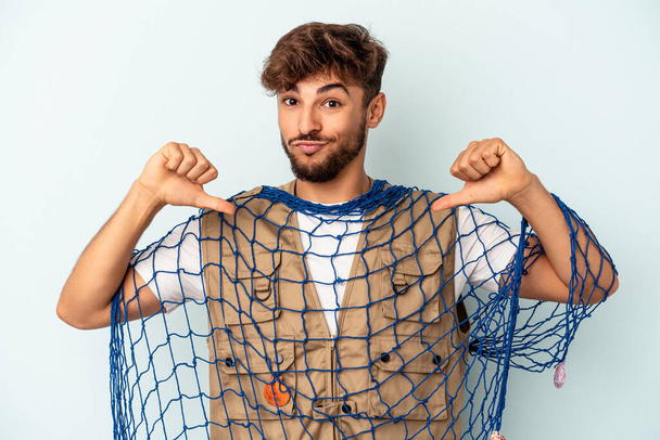Young mixed race fisherman holding a net isolated on blue background feels proud and self confident, example to follow. - Photo, Image