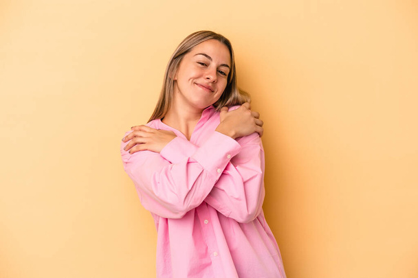 Giovane donna caucasica isolata su sfondo giallo abbracci, sorridente spensierato e felice. - Foto, immagini