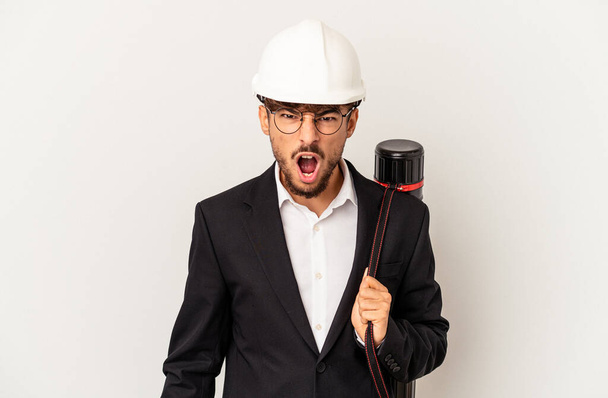 Young mixed race architect man wearing a helmet isolated on grey background screaming very angry and aggressive. - Photo, Image