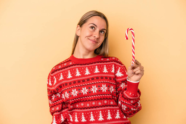 Молода біла жінка тримає різдвяну паличку ізольовано на жовтому тлі мріє досягти цілей і цілей
 - Фото, зображення