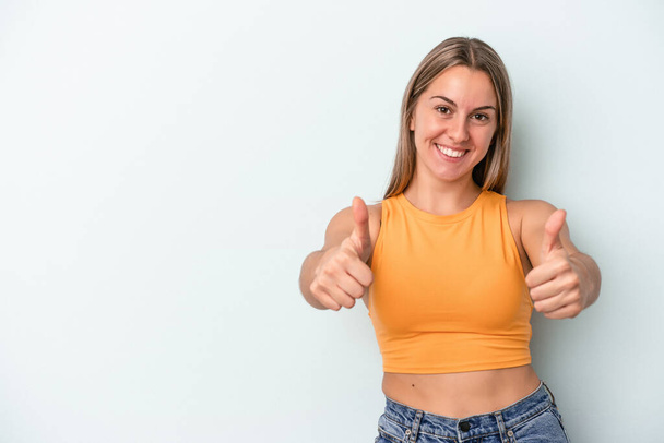 Young caucasian woman isolated on blue background smiling and raising thumb up - Foto, immagini