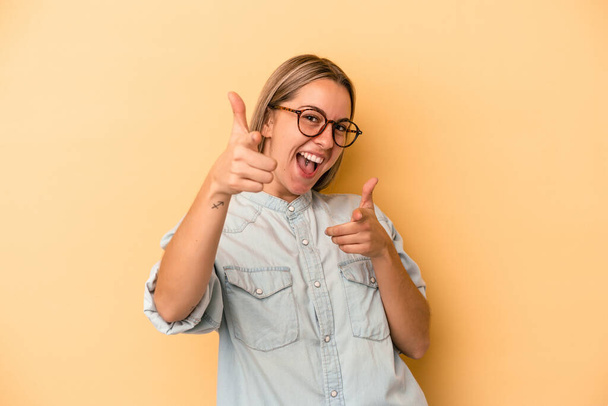 Young caucasian woman isolated on yellow background cheerful smiles pointing to front. - Foto, Imagen