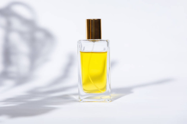 Przezroczysta prostokątna butelka złotych perfum na białym tle ze światłem słonecznym i cieniami liści. Minimalny wzór perfumerii w stylu. Przestrzeń kopiowania - Zdjęcie, obraz