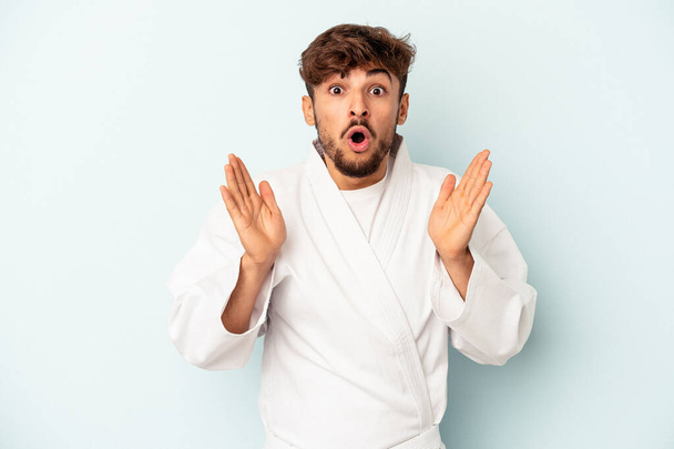 Young mixed race man doing karate isolated on blue background surprised and shocked. - 写真・画像