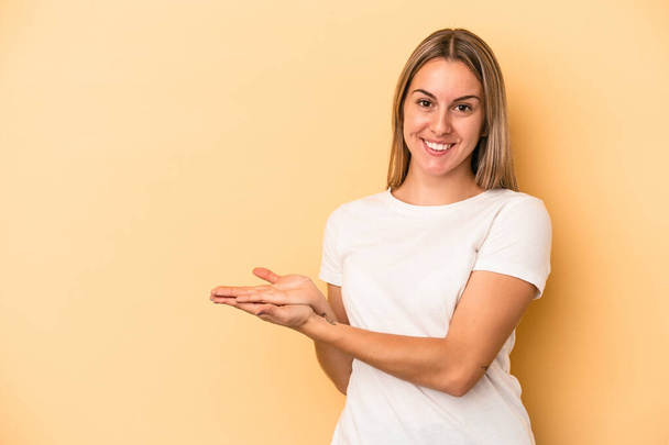 Young caucasian woman isolated on yellow background holding a copy space on a palm. - Foto, imagen