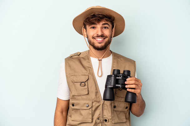 Young mixed race man holding binoculars isolated on blue background happy, smiling and cheerful. - Foto, Bild
