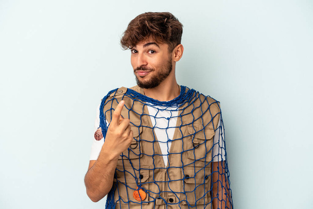 Young mixed race fisherman holding a net isolated on blue background pointing with finger at you as if inviting come closer. - Foto, Imagem