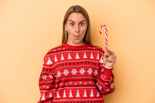 Молода біла жінка тримає різдвяну паличку ізольовану на жовтому тлі соломинки на плечах і розгублених очах
. - Фото, зображення