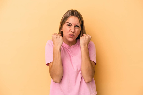 Young caucasian woman isolated on yellow background showing fist to camera, aggressive facial expression. - Foto, Imagem