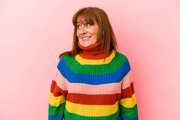 Middle age caucasian woman wearing a multicolor sweater isolated on pink background looks aside smiling, cheerful and pleasant. - Foto, Bild